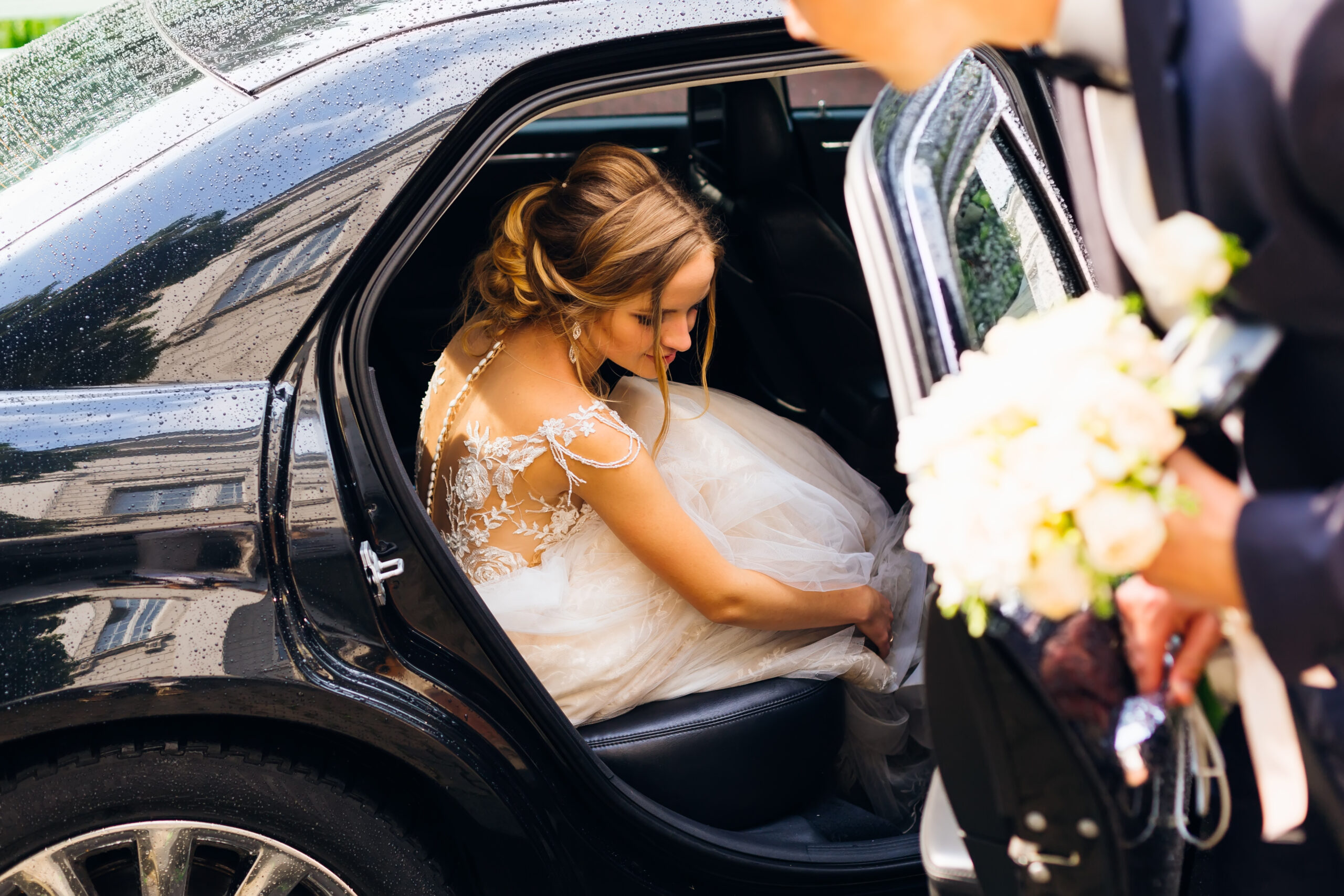 the beautiful bride sits in a black car and the groom wants to close the door after
